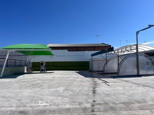 Carpa textil verde instalada sobre una zona de autolavado con equipos de lavado para coches.