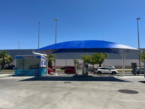 Marquesina textil azul instalada en una zona exterior de autolavado con vehículos alrededor